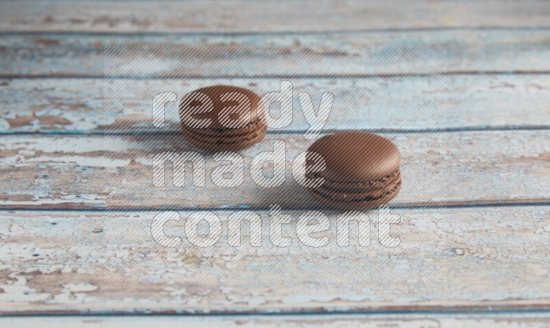 45º Shot of two Brown Dark Chocolate macarons on light blue wooden background