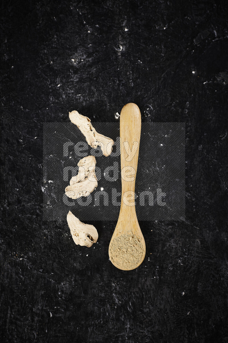 A wooden spoon full of ground ginger powder on black background