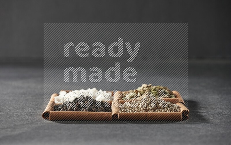 4 squares of cinnamon sticks full of black pepper, white pepper, cardamom and white salt on black flooring