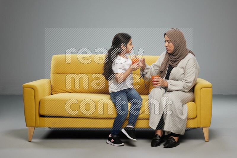 Mom and daughter sitting drinking juice on gray background