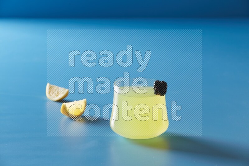 glass of lemon juice with berry on blue background