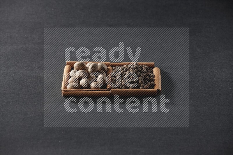 مربعان من أعواد القرفة ممتلئان بجوزة الطيب وحبوب الفلفل الحلو علي خلفية سوداء