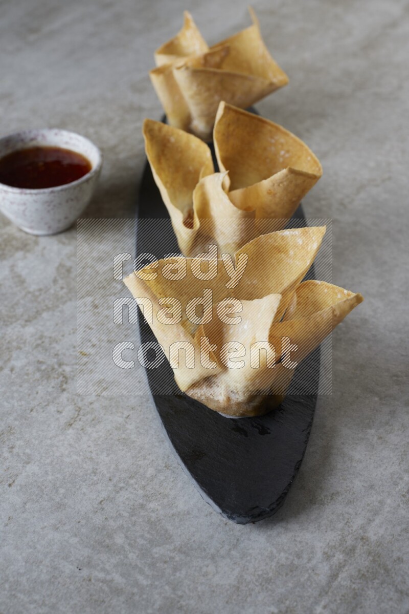 wonton cups with soy sauce ramkin on oval slate on grey textured counter top
