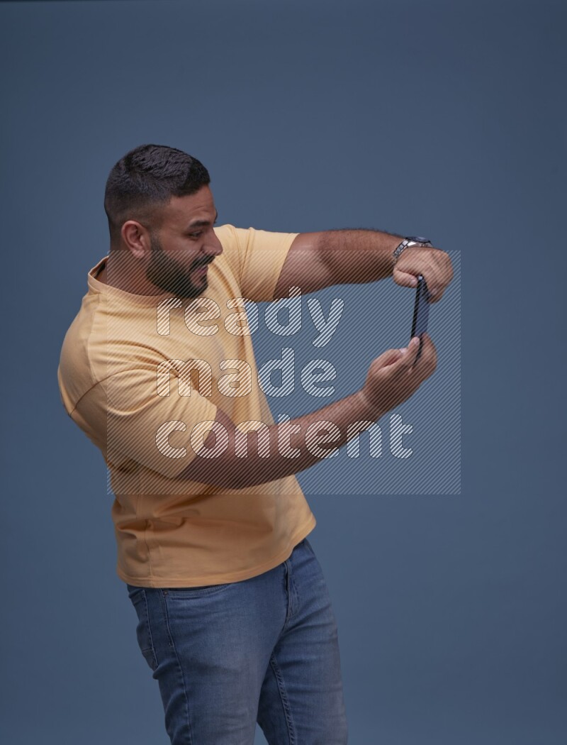 A man Playing Games on Smartphone on Blue Background wearing Orange T-shirt