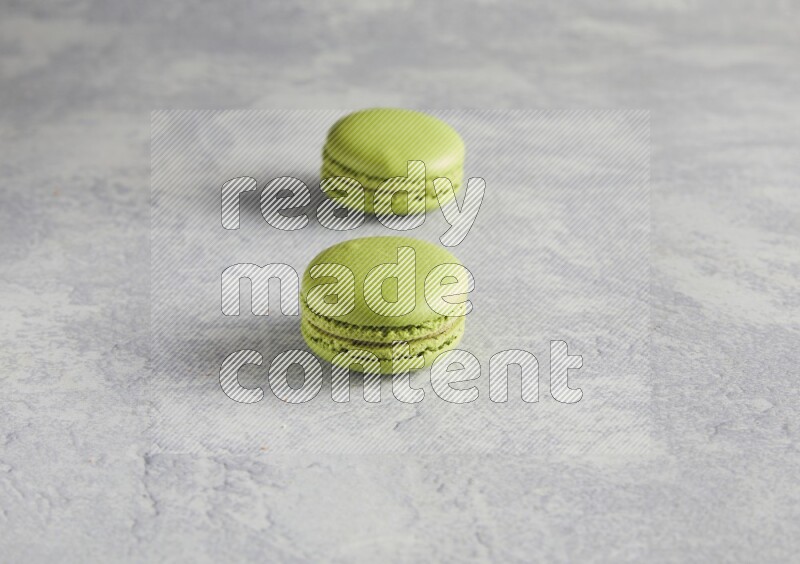 45º Shot of two Green Pistachio macarons  on white  marble background