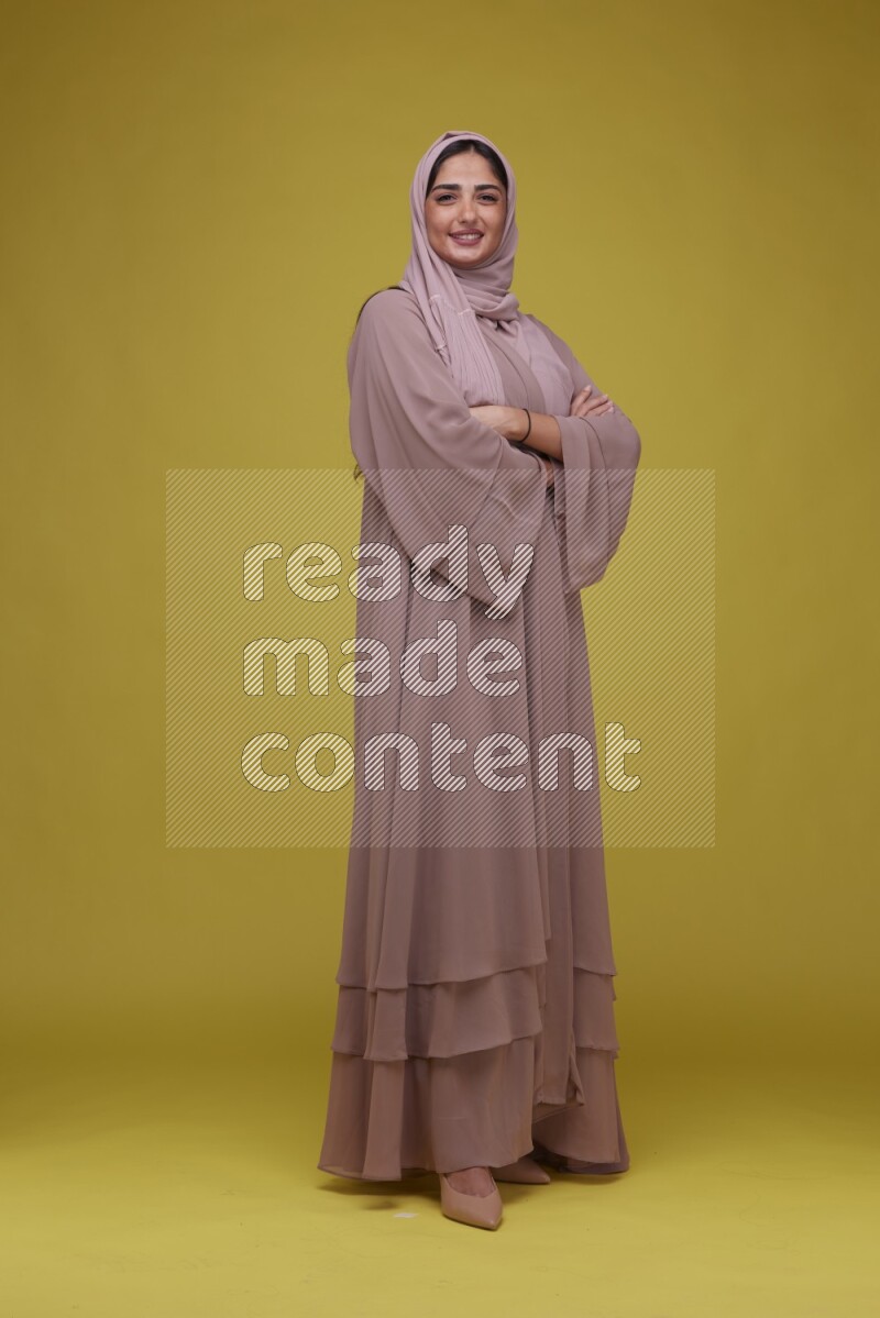 A woman Posing on a Yellow Background wearing Brown Abaya with Hijab