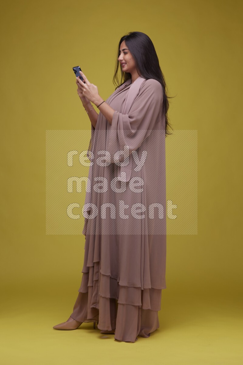 A woman Texting on a Yellow Background wearing Brown Abaya