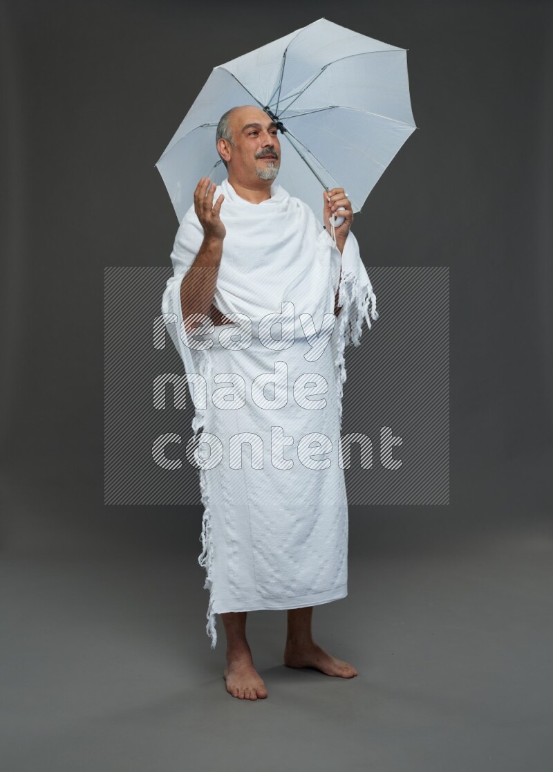 A man wearing Ehram Standing holding umbrella on gray background