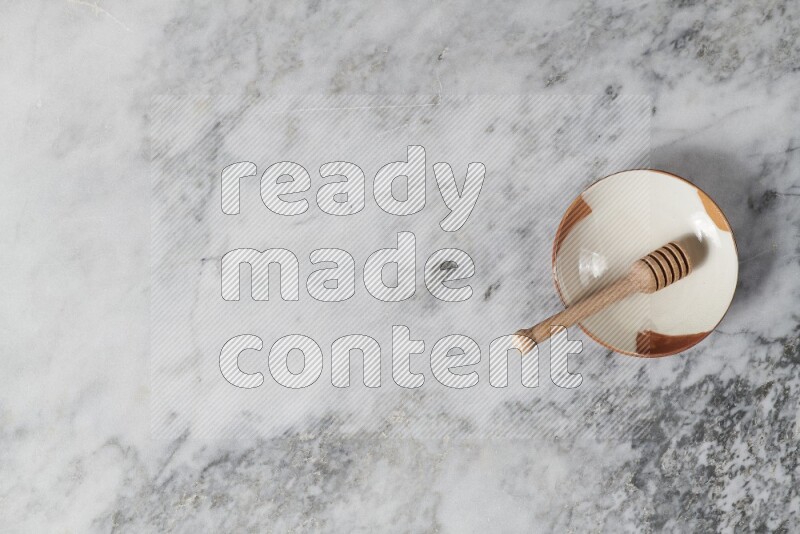 طبق فخاري متعدد الألوان مع ملعقة عسل خشبية بداخله على خلفية من الرخام الرمادي