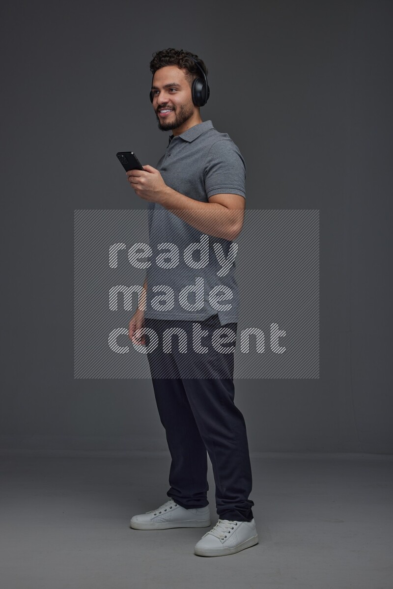 A man wearing casual and using his phone and headphone eye level on a gray background