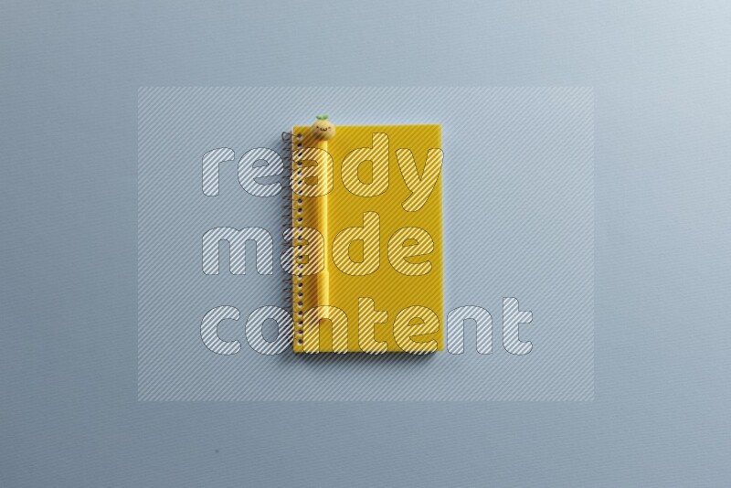 A yellow notebook with different school supplies on blue background