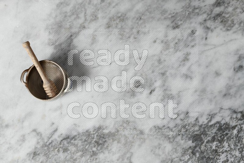 وعاء فخاري متعدد الألوان مع ملعقة عسل خشبية بداخله على خلفية من الرخام الرمادي