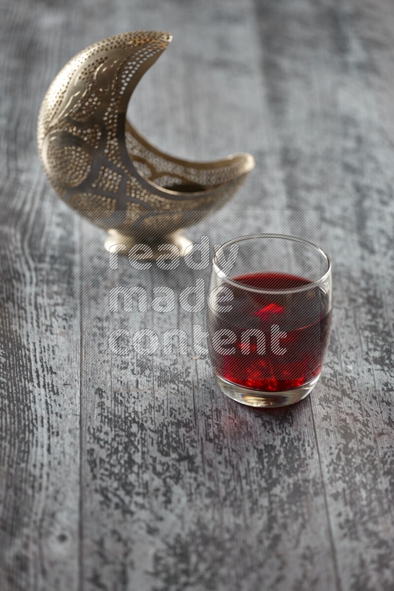 A silver lantern with different drinks, dates, nuts, prayer beads and quran on grey wooden background