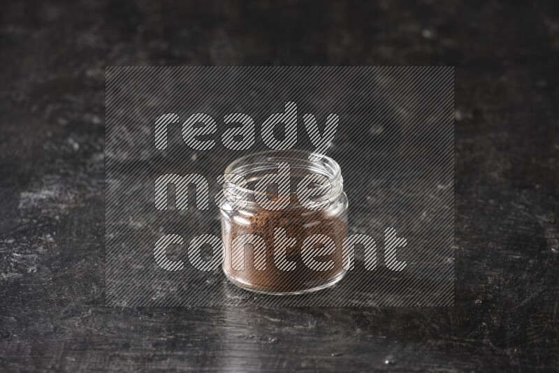 A glass jar full of cloves powder on a textured black flooring