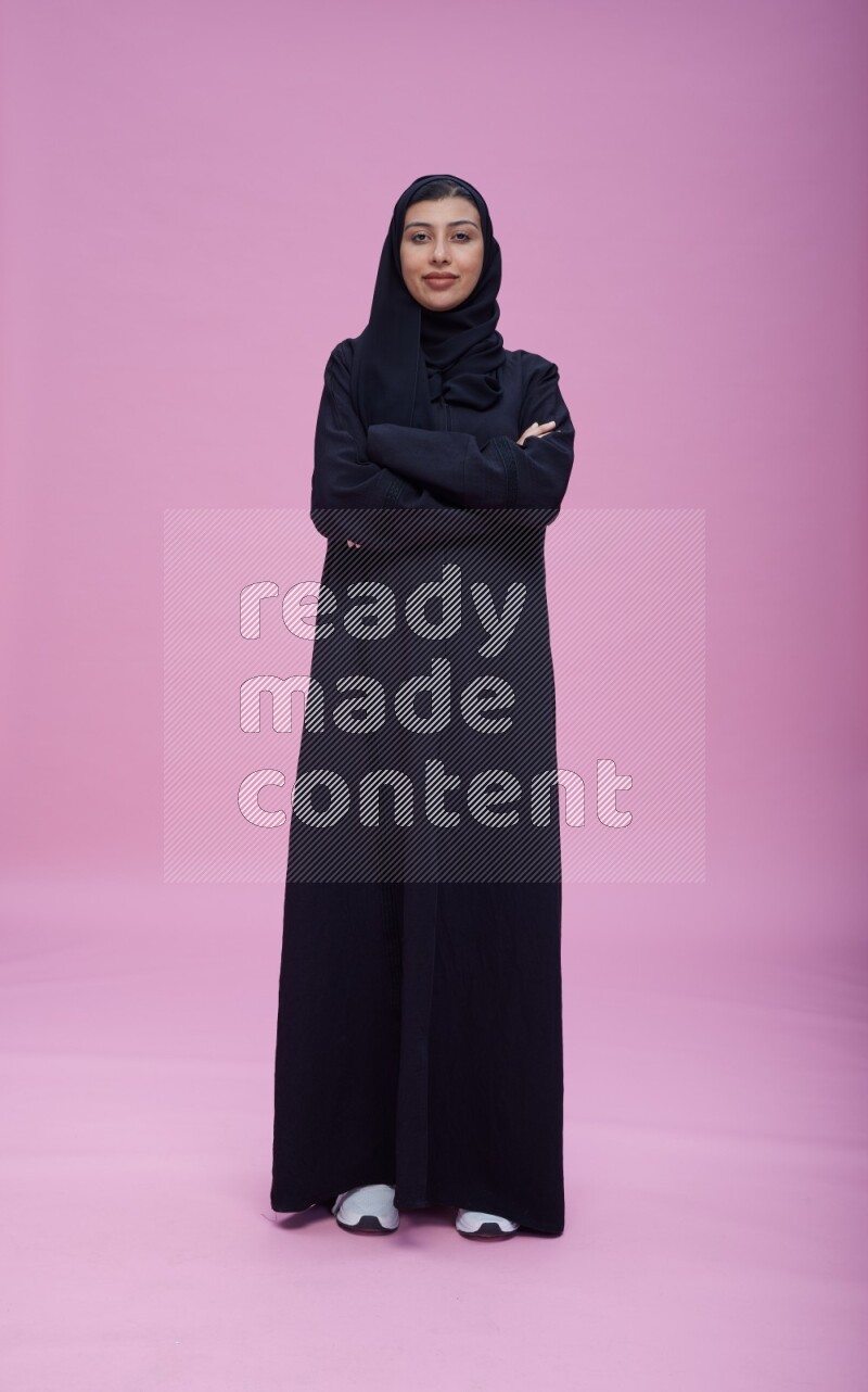 Saudi woman wearing Abaya standing with crossed arms on pink background
