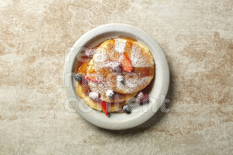 Three stacked mixed berries pancakes in a grey plate on beige background
