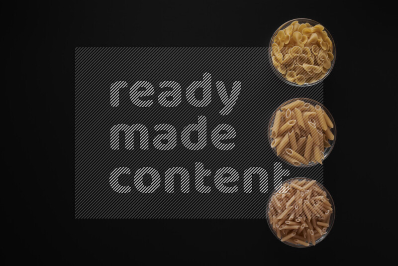 Different pasta types in 3 glass bowls on black background