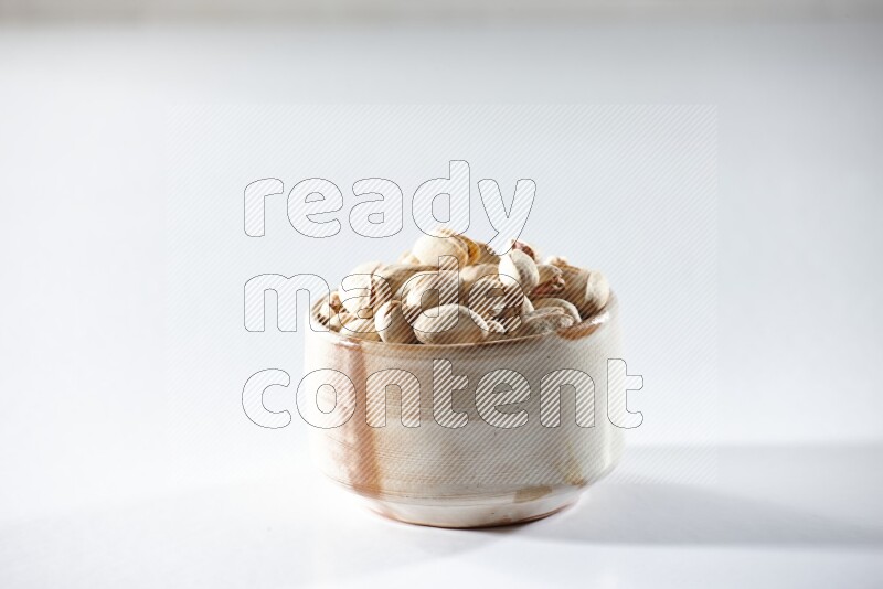 A beige ceramic bowl full of pistachios on a white background in different angles