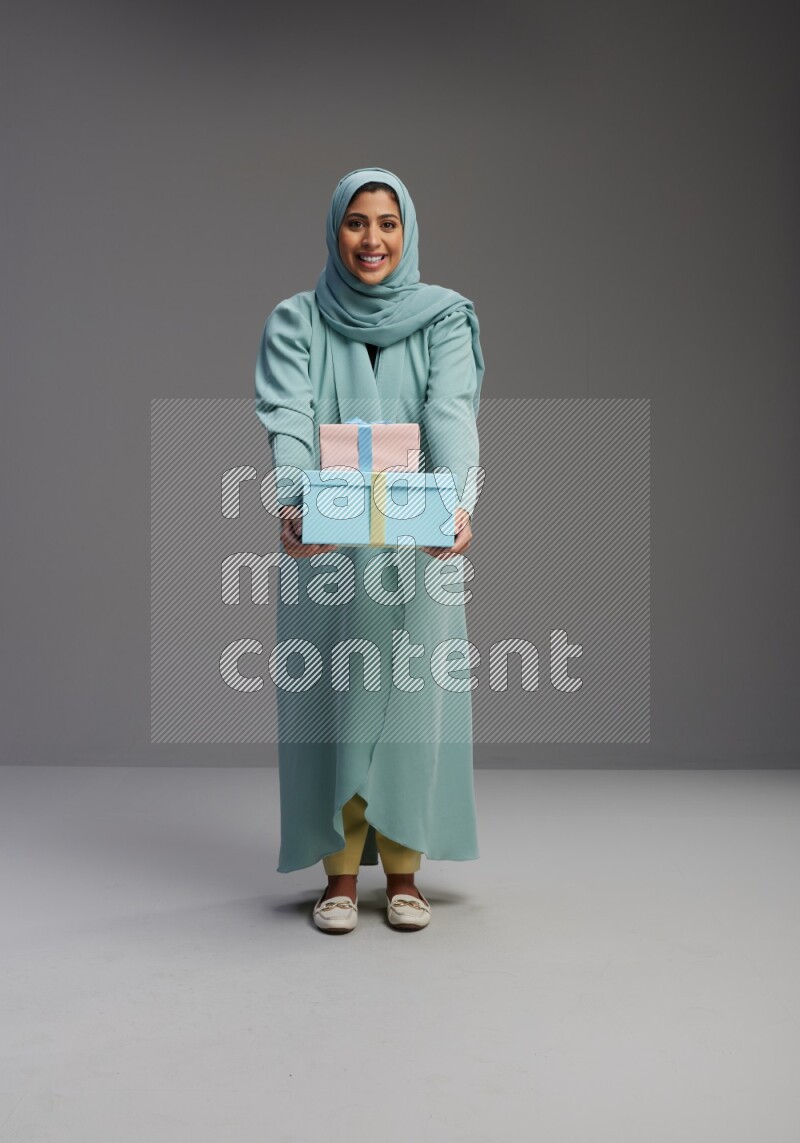 Saudi Woman wearing Abaya standing holding gift box on Gray background