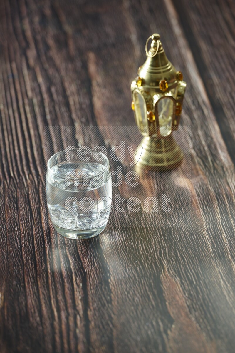 A golden lantern with different drinks, dates, nuts, prayer beads and quran on brown wooden background