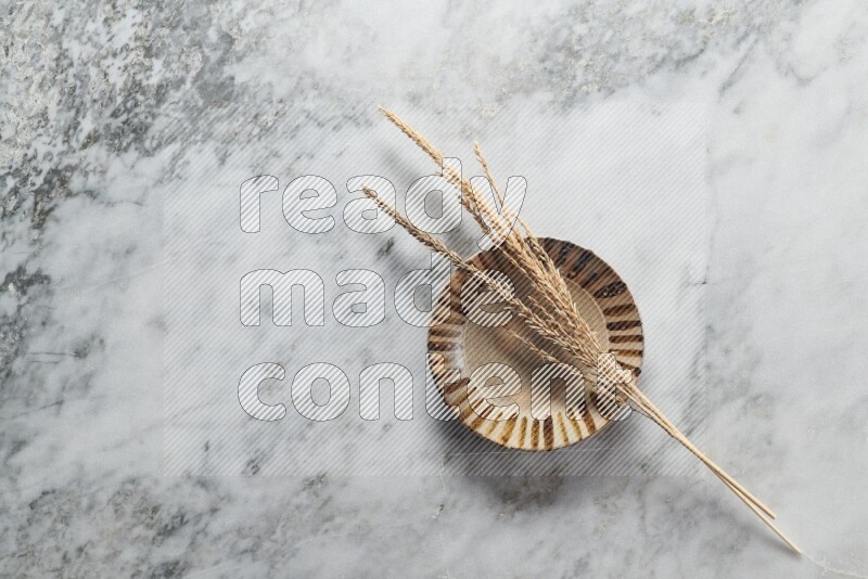Wheat stalks on multicolored pottery plate on grey marble background