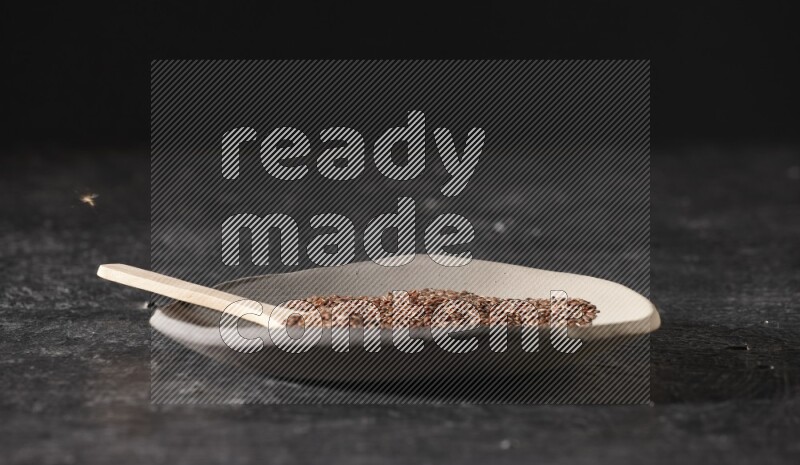 A multicolored pottery plate full of flaxseeds and wooden spoon full of seeds on a textured black flooring