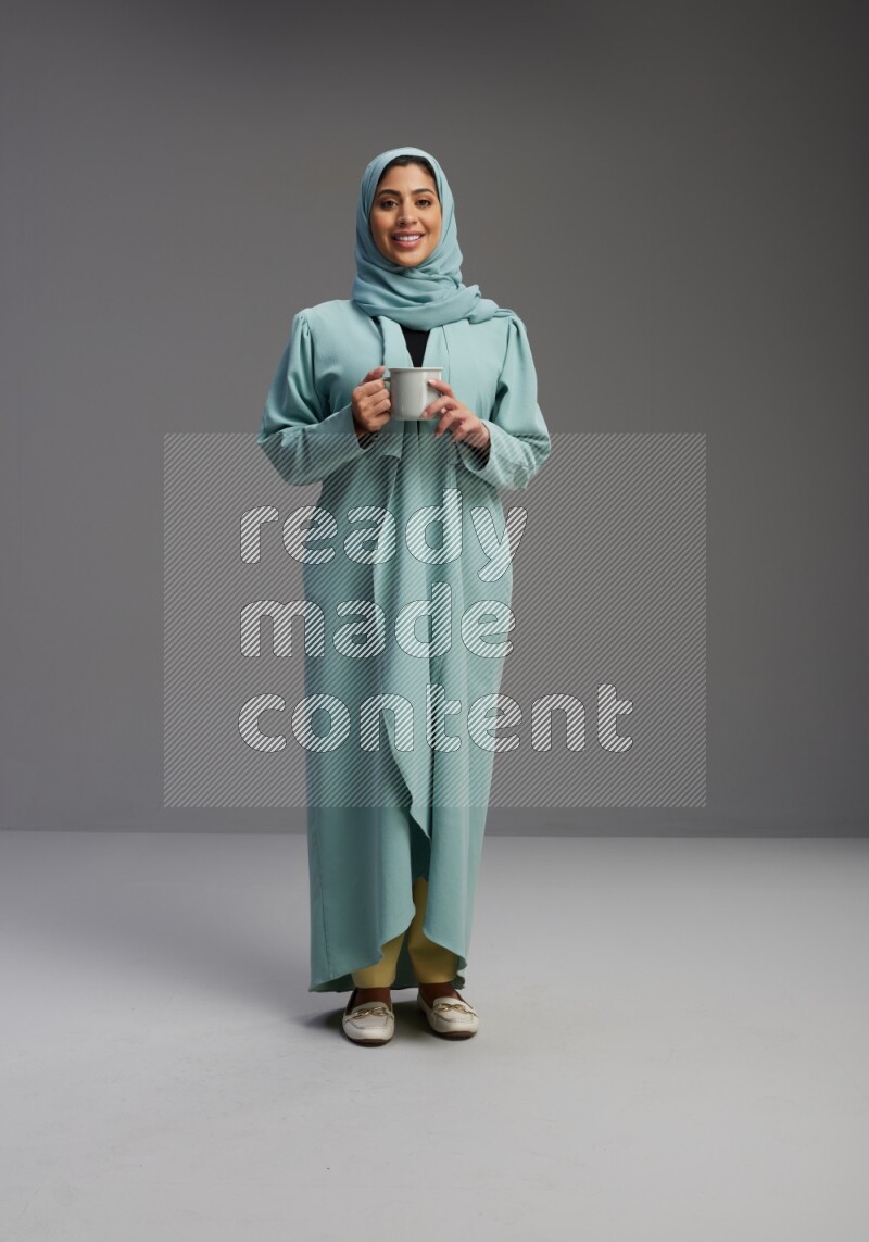 Saudi Woman wearing Abaya standing  holding a mug on Gray background