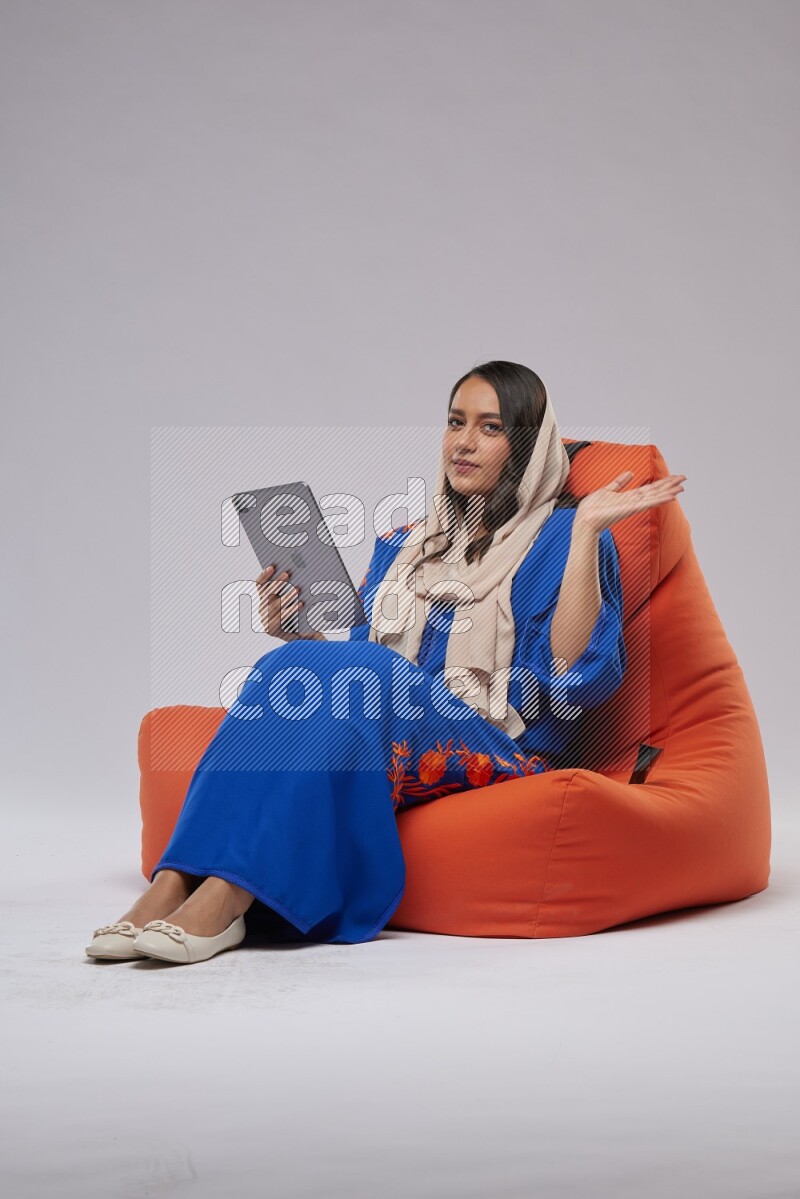 A Saudi woman sitting on an orange beanbag and working on tablet