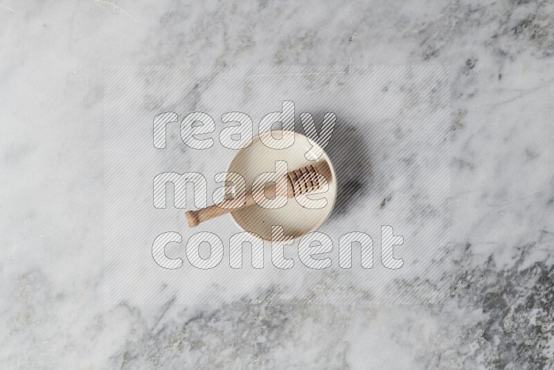 Beige pottery bowl with wooden honey dipper in it on grey marble background