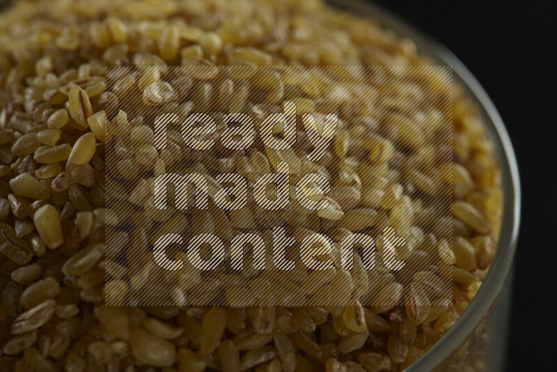 Coarse bulgur in a glass jar on black background