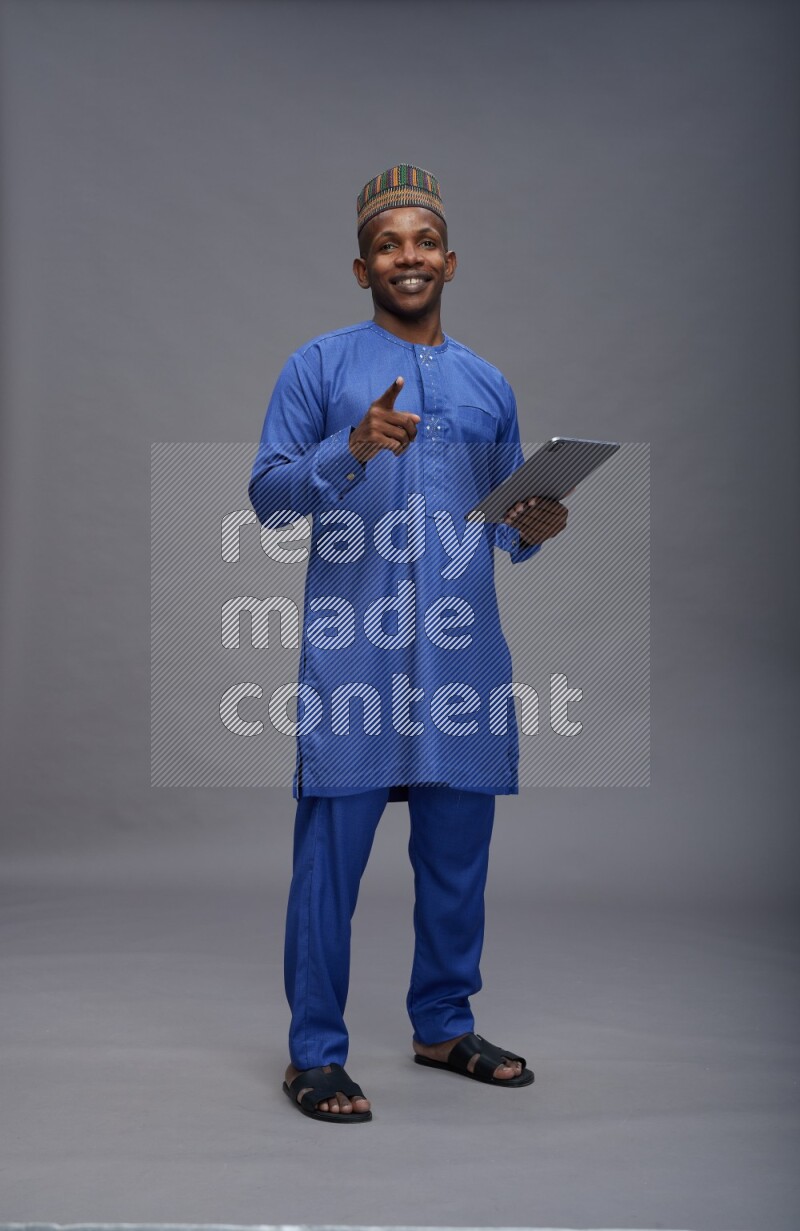 Man wearing Nigerian outfit standing working on tablet on gray background