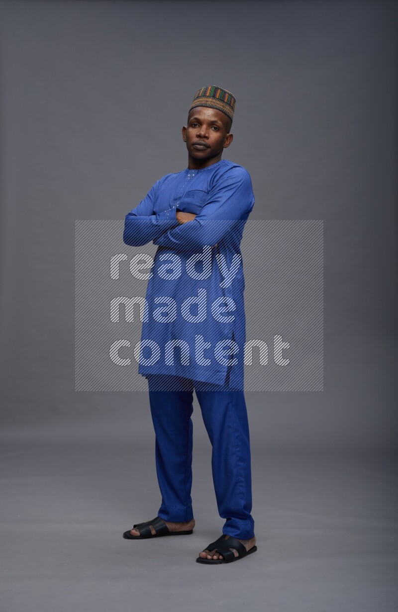 Man wearing Nigerian outfit standing with crossed arms on gray background