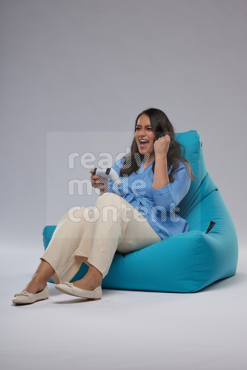 A woman sitting on a blue beanbag and gaming with joystick