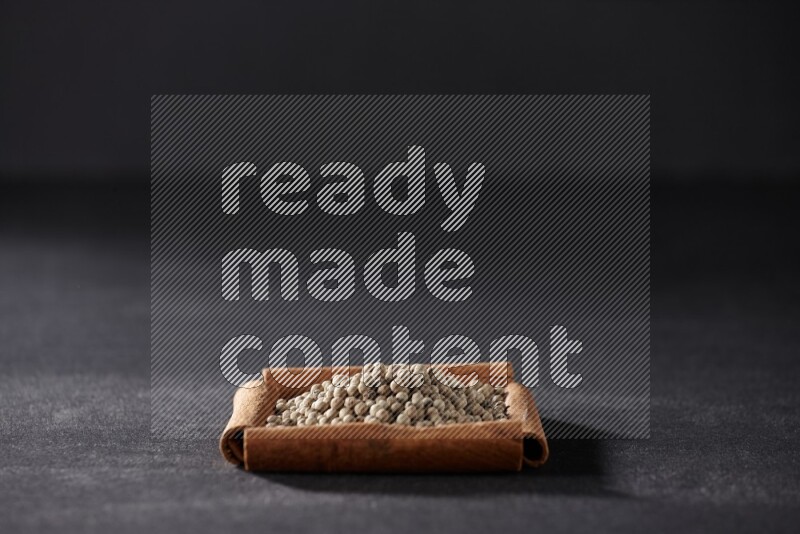 أربعة من أعواد القرفة مكونة شكل مربع بداخلها حبوب الفلفل الأبيض علي خلفية سوداء