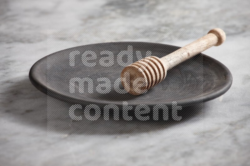 Black pottery plate with wooden honey dipper in it on grey marble background