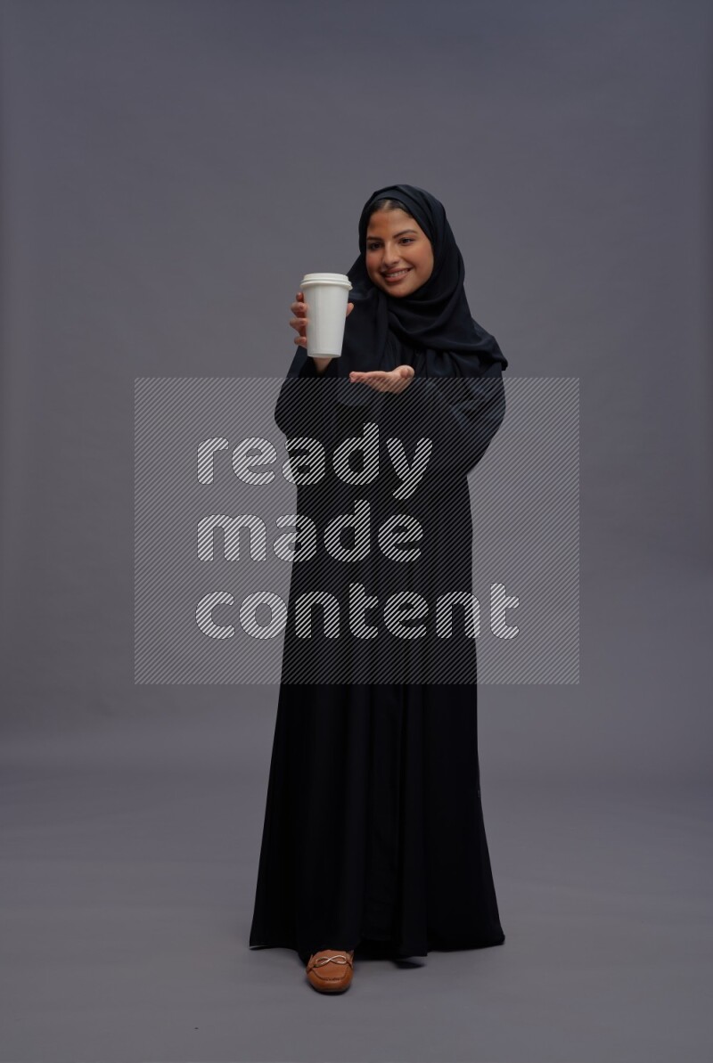 Saudi woman wearing Abaya standing holding paper cup on gray background