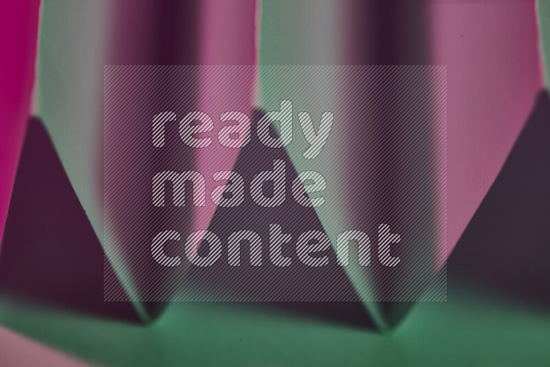 A close-up abstract image showing sharp geometric paper folds in green and pink gradients