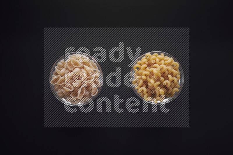Different pasta types in glass bowls on black background