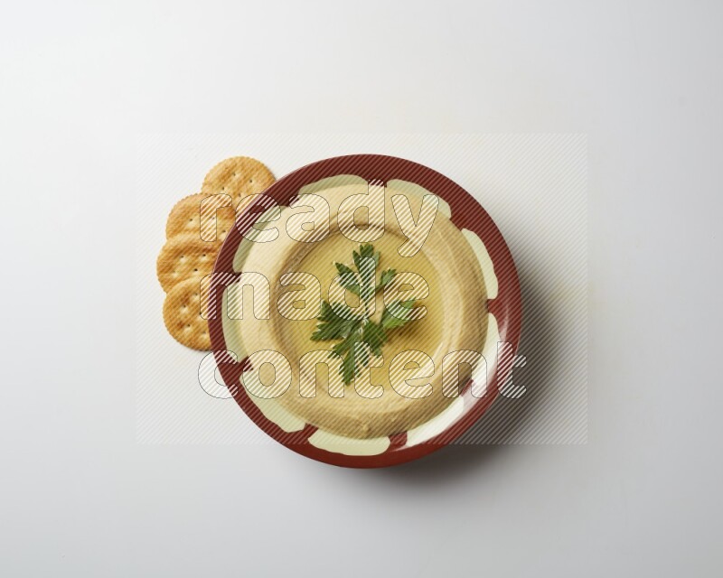 Hummus in a traditional plate garnished with parsley on a white background