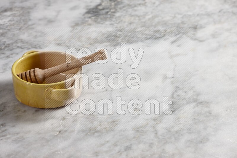 Multicolored pottery bowl with wooden honey dipper in it on grey marble background