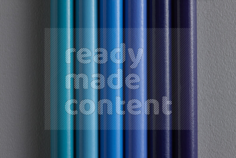 A collection of colored pencils arranged showcasing a gradient of blue hues on grey background