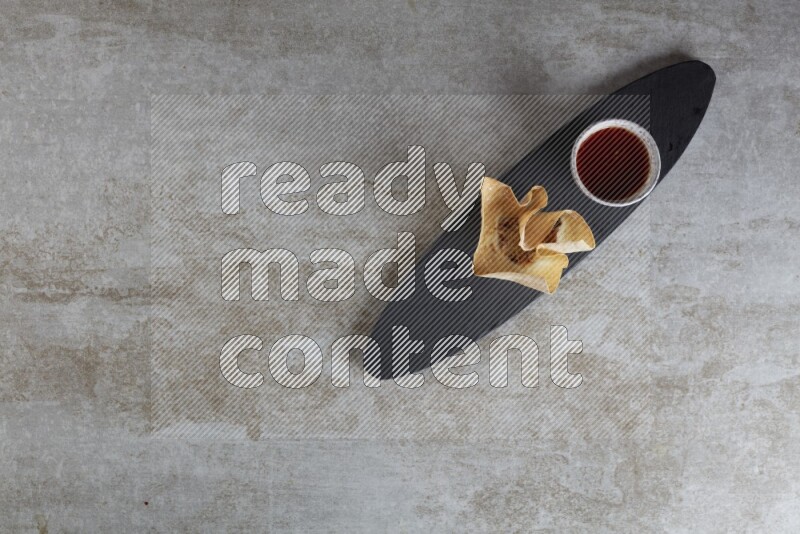 wonton cups with soy sauce ramkin on oval slate on grey textured counter top