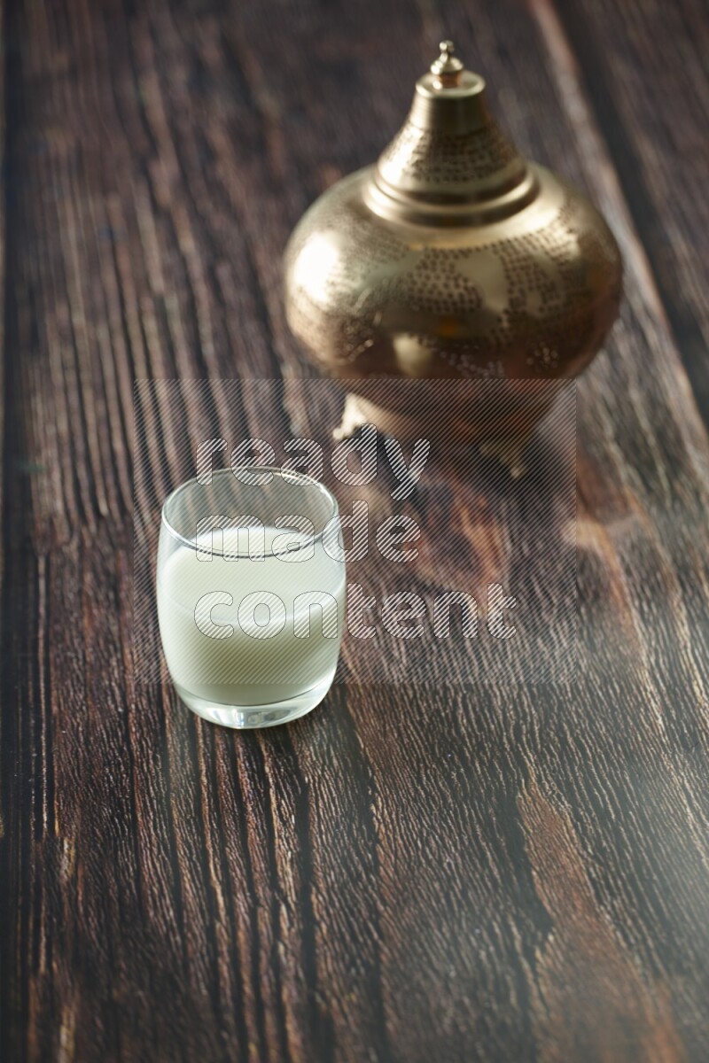 A golden lantern with different drinks, dates, nuts, prayer beads and quran on brown wooden background