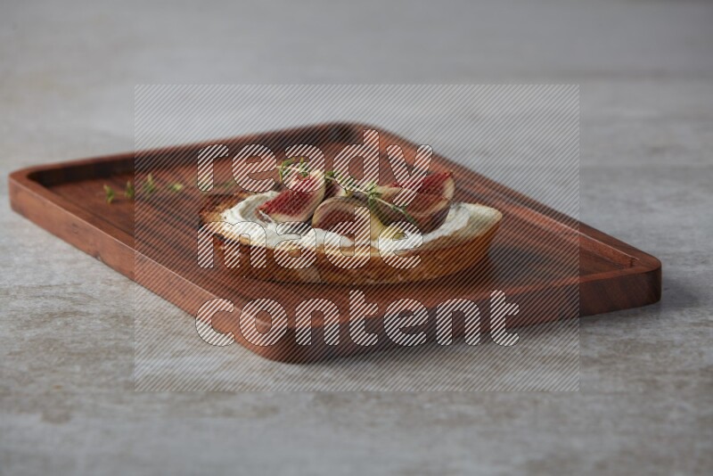 quarters of figs with cream cheese on toasted sourdough slice on a wooden board on textured grey background