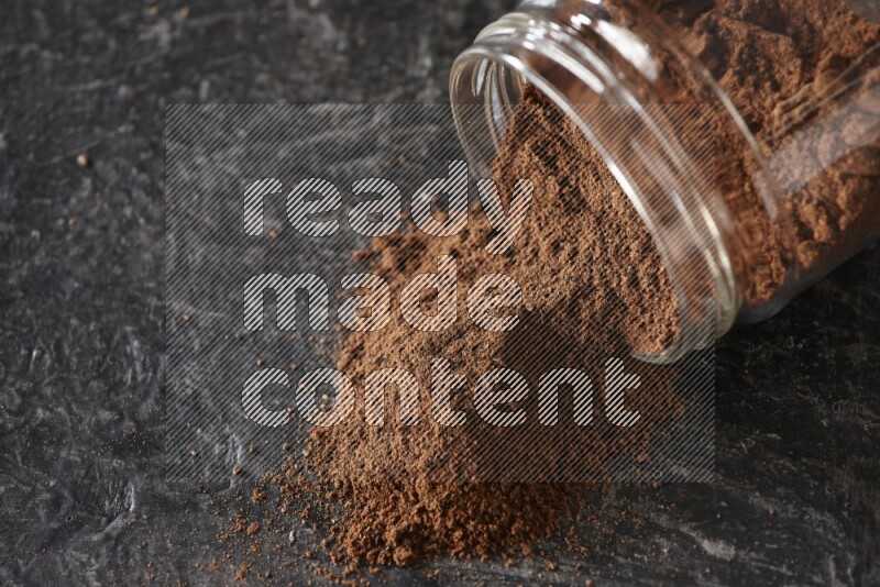 A flipped glass jar full of cloves powder on a textured black flooring