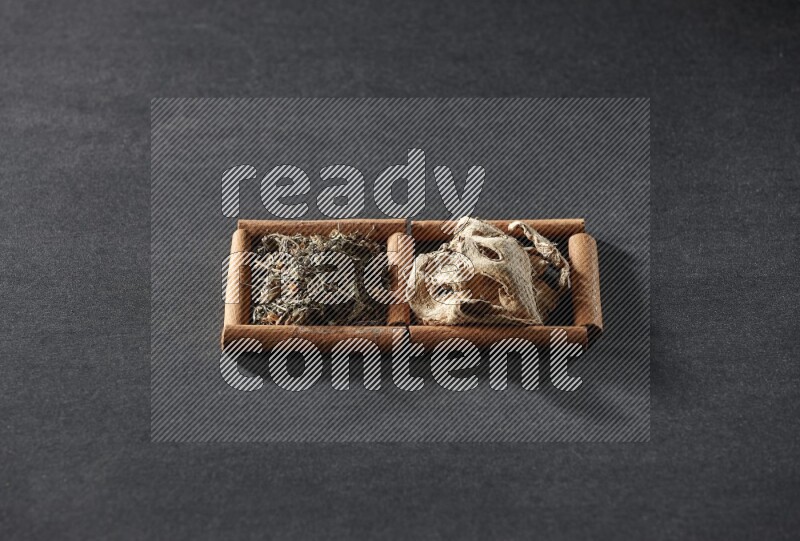 مربعان من أعواد القرفة ممتلئان بالزنجبيل المجفف والريحان المجفف علي خلفية سوداء