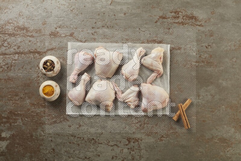 Mixed fresh chicken pieces on a parchment paper direct on a textured rustic background