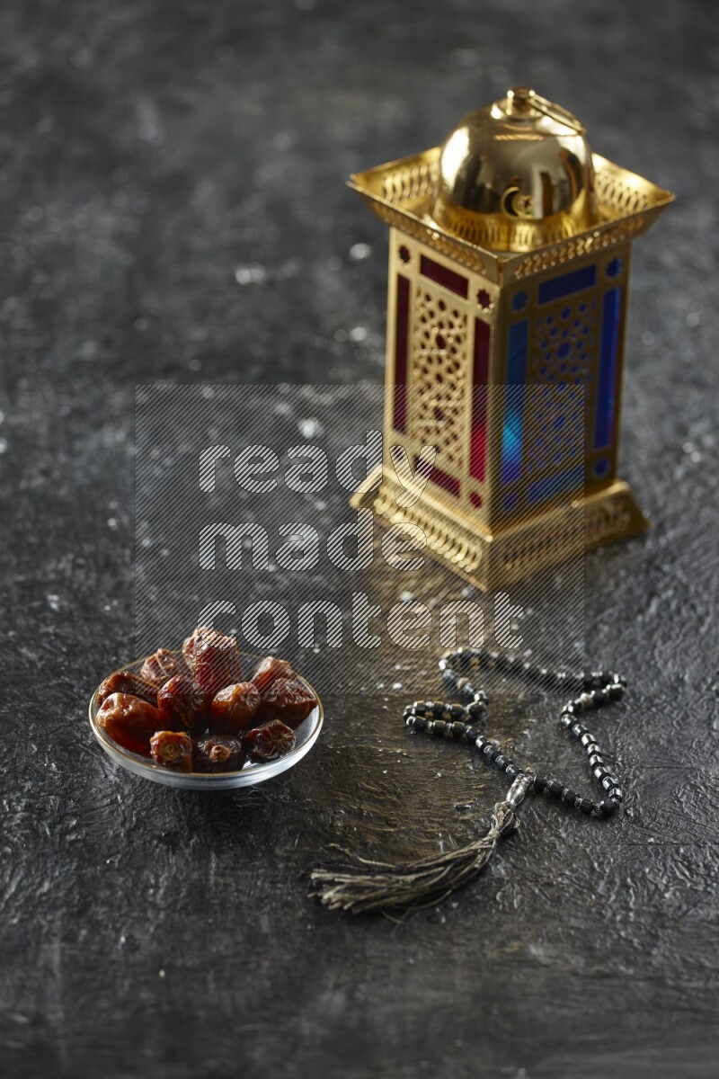 A golden lantern with different drinks, dates, nuts, prayer beads and quran on textured black background