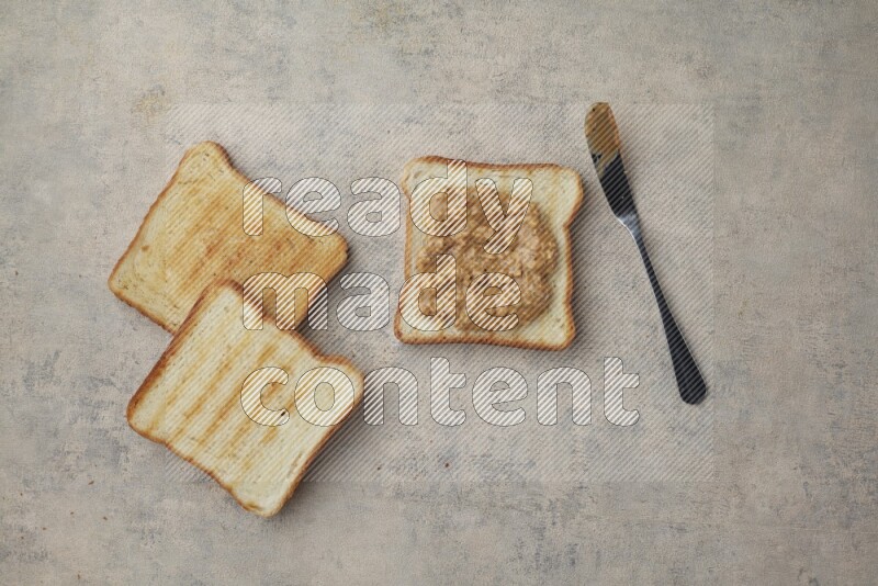 Crunchy peanut butter on a toasted white toast and toasted white toast slices on a light blue textured background