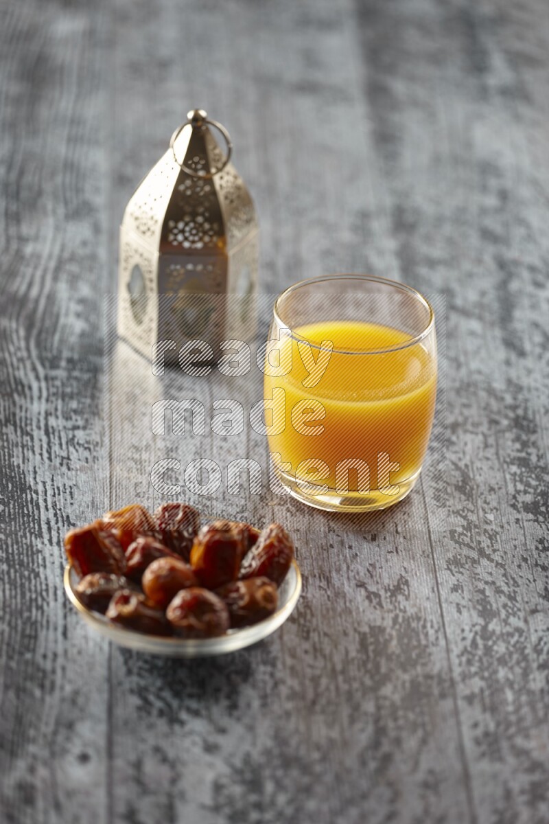 فانوس فضي مع مشروبات مختلفة وتمر ومكسرات وسبحة صلاة وقرآن على خلفية خشبية رمادية